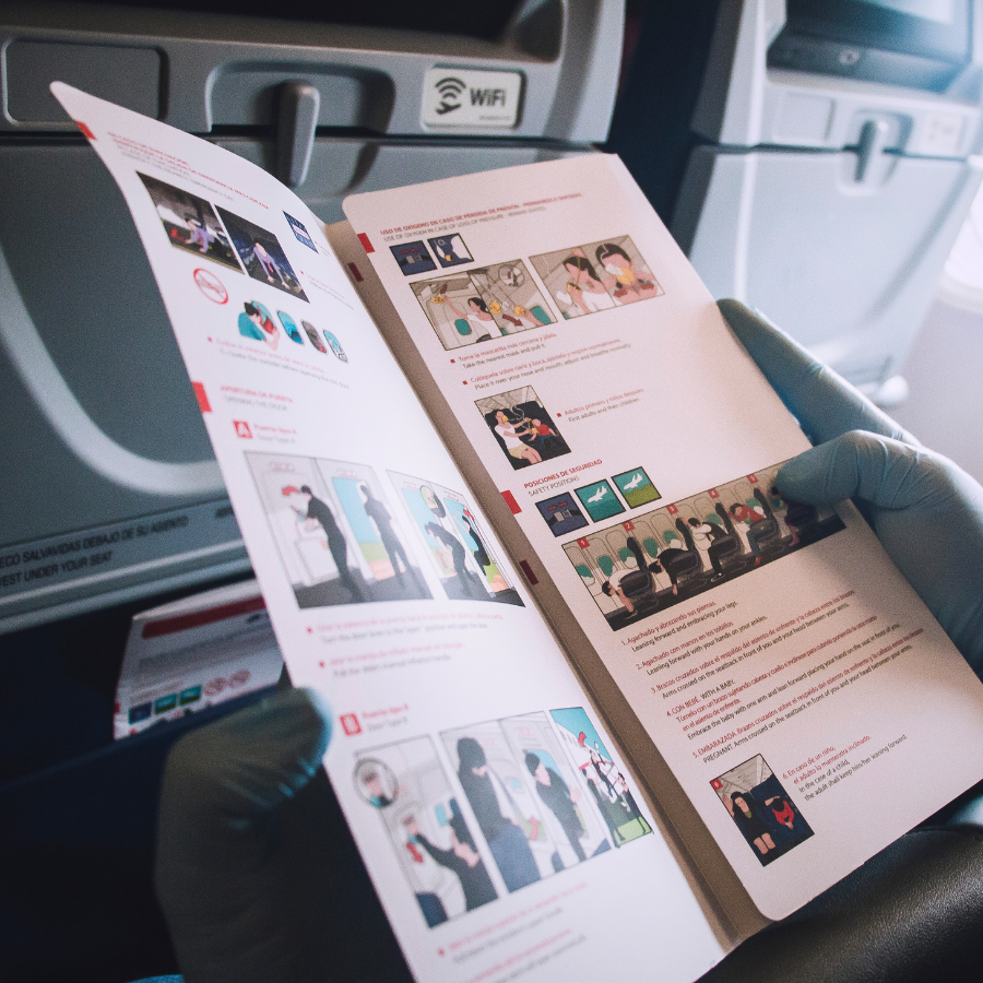 Person in blue gloves holding an open airplane safety brochure, inside an airplane.