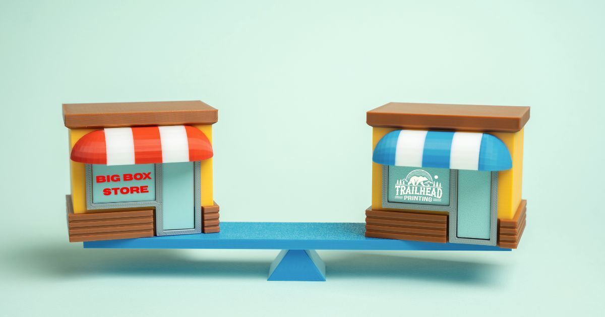 Two tiny storefronts on a blue seesaw, one red-and-white, one blue-and-white, against a light background