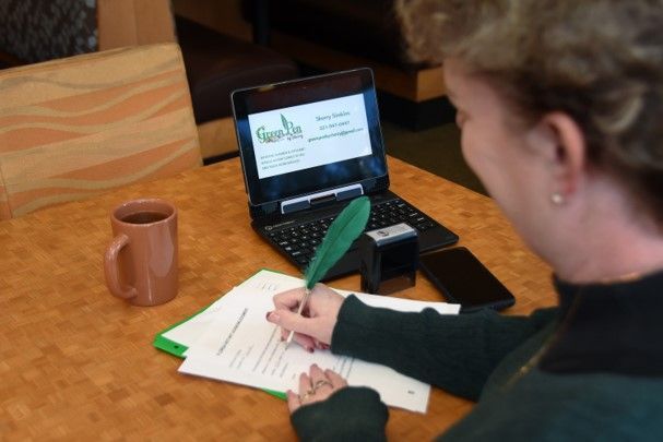 A woman is writing on a piece of paper in front of a laptop.