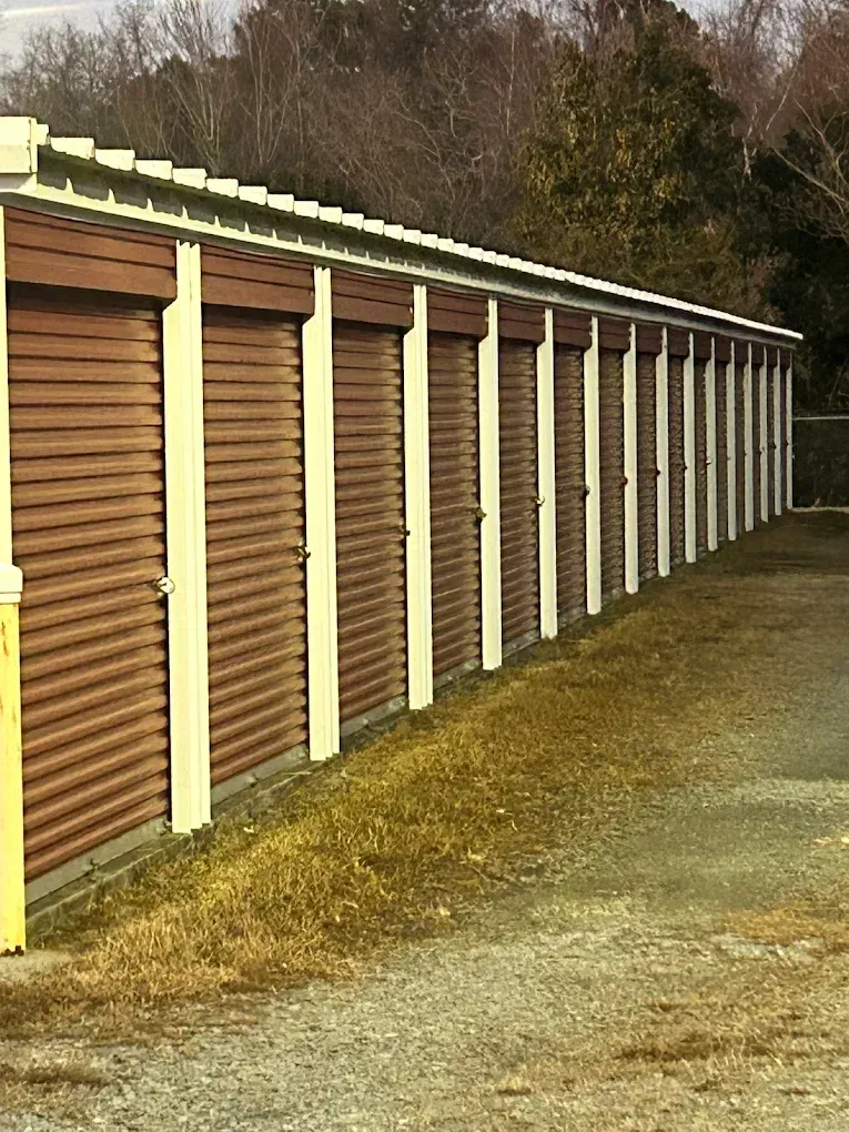 Brown storage units with white trim, located outdoors, along a gravel path.