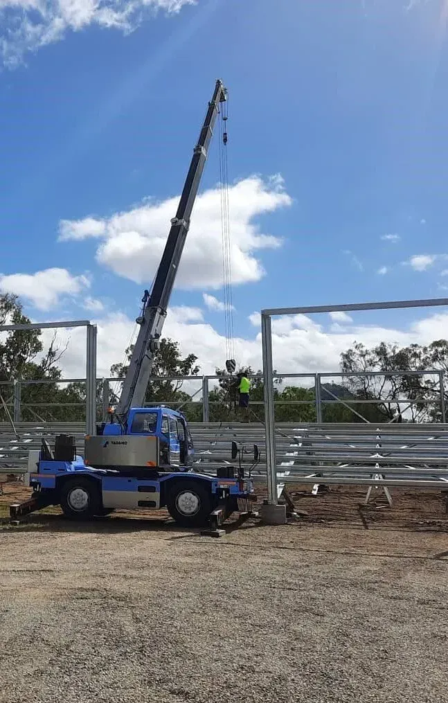 A Blue Crane Lifts a Steel Frame Into Place at a Construction Site — Presto's Cranes & Rigging NQ in Garbutt, QLD