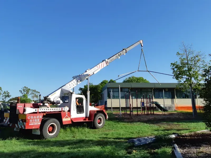 Crane Lifting a Structure Over a School Building With a Playground — Presto's Cranes & Rigging NQ in Garbutt, QLD