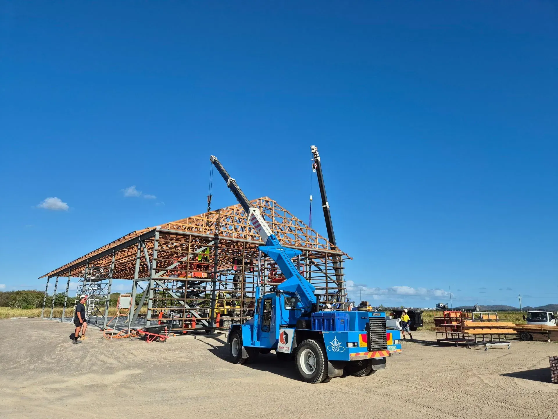 Blue Crane Lifting Roof Trusses on a Building Frame Under Construction — Presto's Cranes & Rigging NQ in Garbutt, QLD