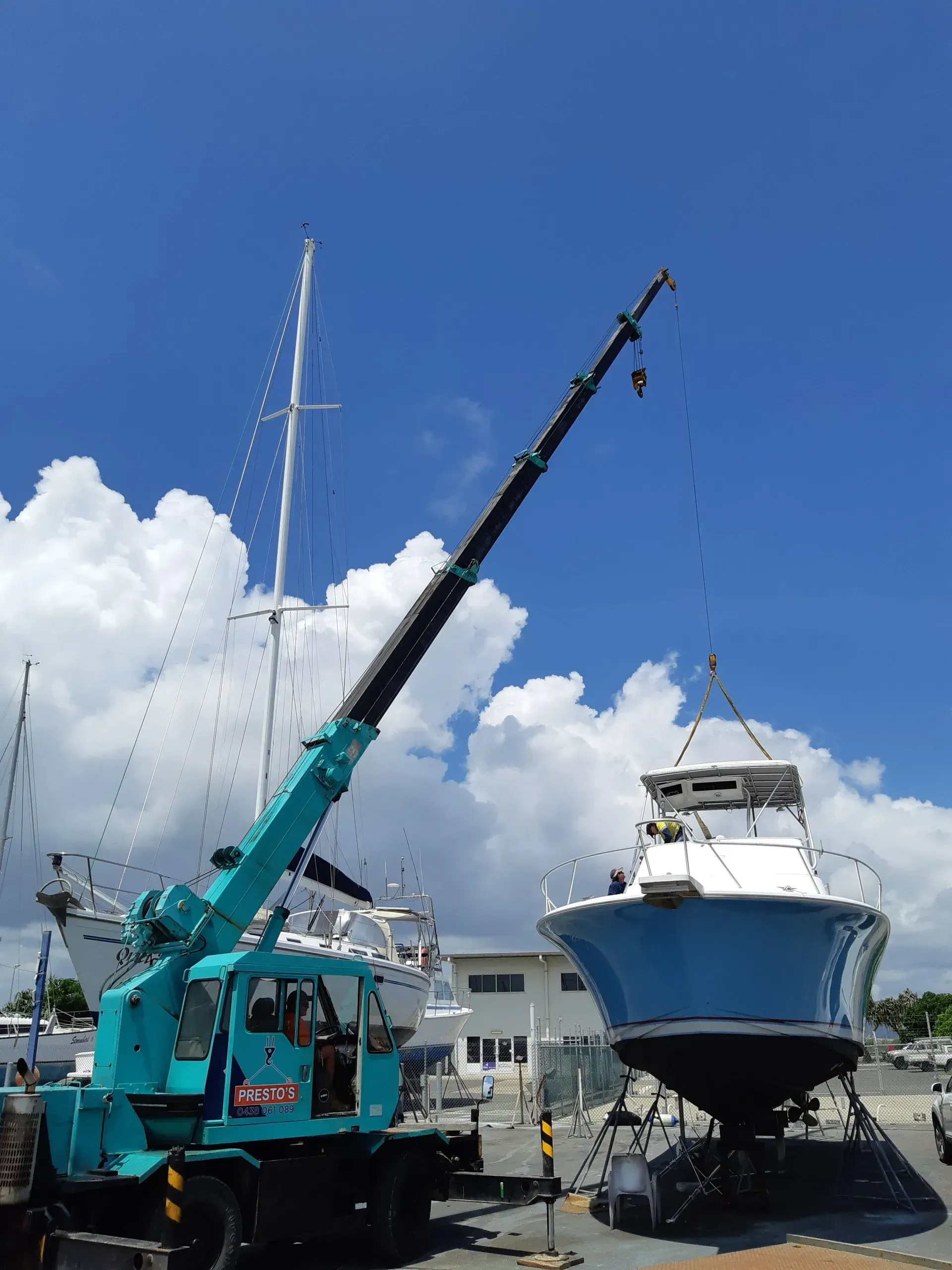 A Blue Boat Being Lifted by a Teal Crane at a Marina — Presto's Cranes & Rigging NQ in Garbutt, QLD