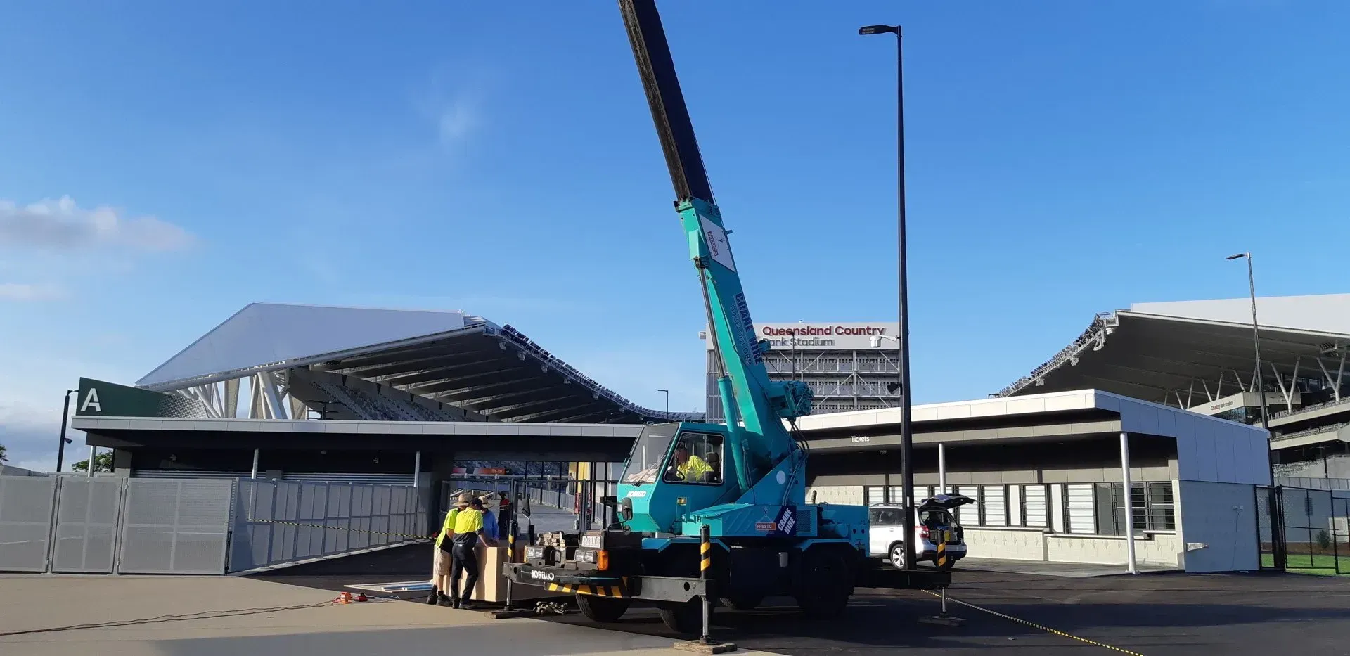 A Teal Crane Near a Building With Two Workers — Presto's Cranes & Rigging NQ in Garbutt, QLD
