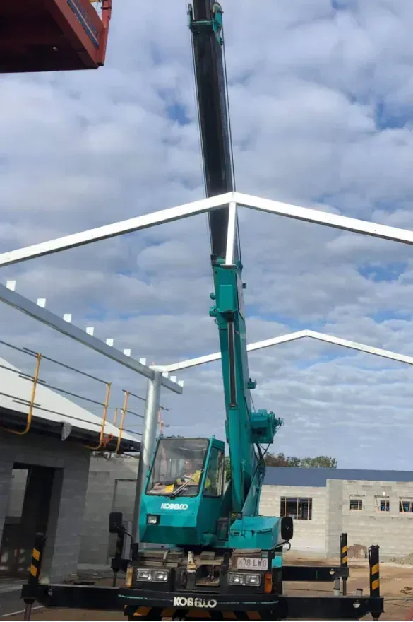 A Teal Crane Lifting a Metal Beam Into a Building Frame — Presto's Cranes & Rigging NQ in Garbutt, QLD