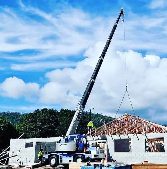 Crane Lifting Roof Trusses Onto a Building Under Construction — Presto's Cranes & Rigging NQ in Garbutt, QLD