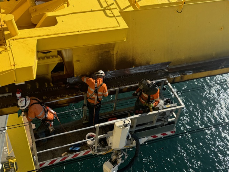 A Group Of Men Are Working On A Large Yellow Ship In The Ocean — JMG Maintenance & Fabrication In Muswellbrook NSW