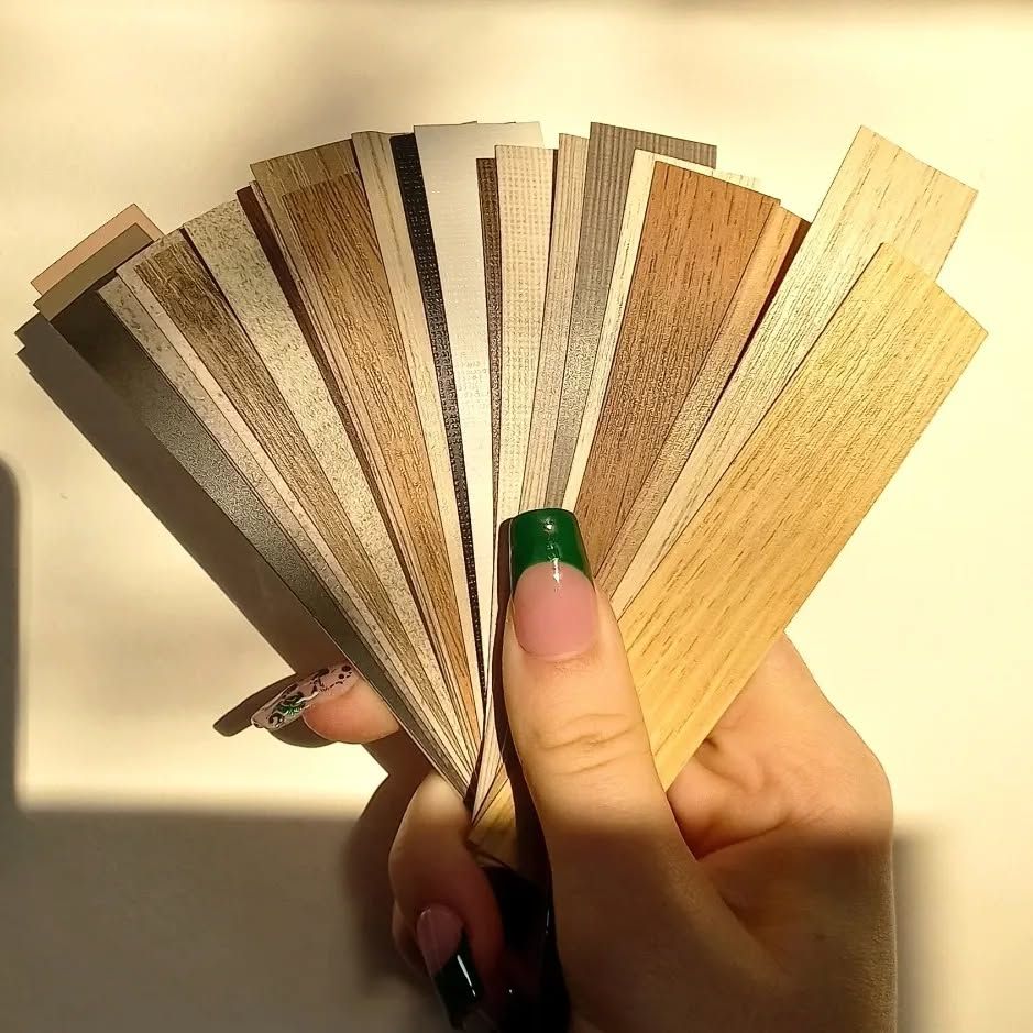 Una mujer con uñas verdes sostiene un abanico con muestras de madera.