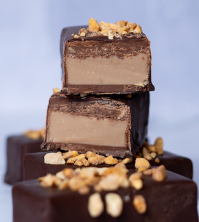 Trozos de chocolate apilados, uno de ellos cortado para revelar capas de relleno y cubierto con nueces picadas.