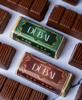 Dos barras de chocolate de Dubai con detalles dorados, rodeadas de otras piezas de chocolate.