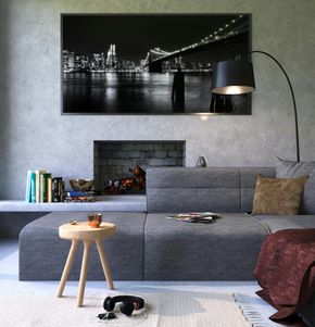 Moderna sala de estar con un sofá seccional gris, chimenea, fotografía de un paisaje urbano y una pequeña mesa auxiliar de madera con auriculares.