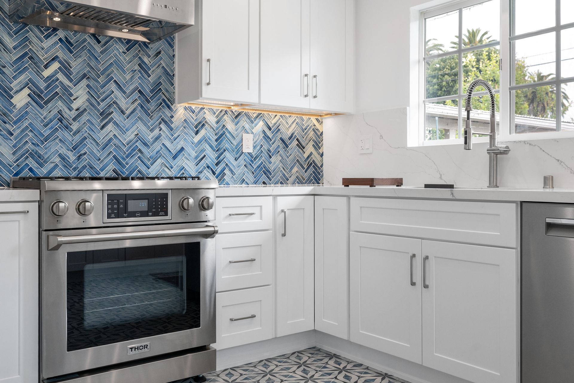 Bright white kitchen with stainless steel appliances and blue herringbone backsplash.
