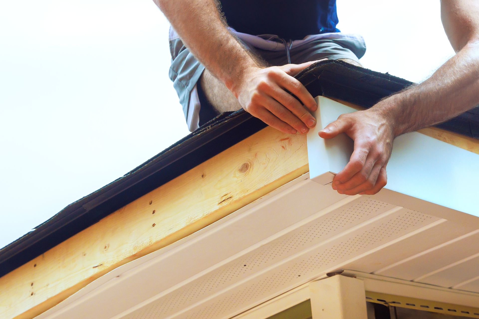 Person installing white siding on a house roof, hands visible, outdoors.