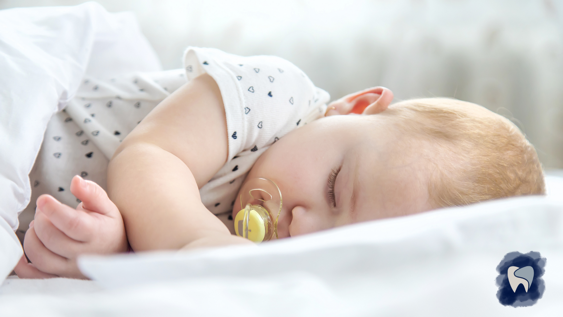 A baby with a pacifier is sleeping on a bed.