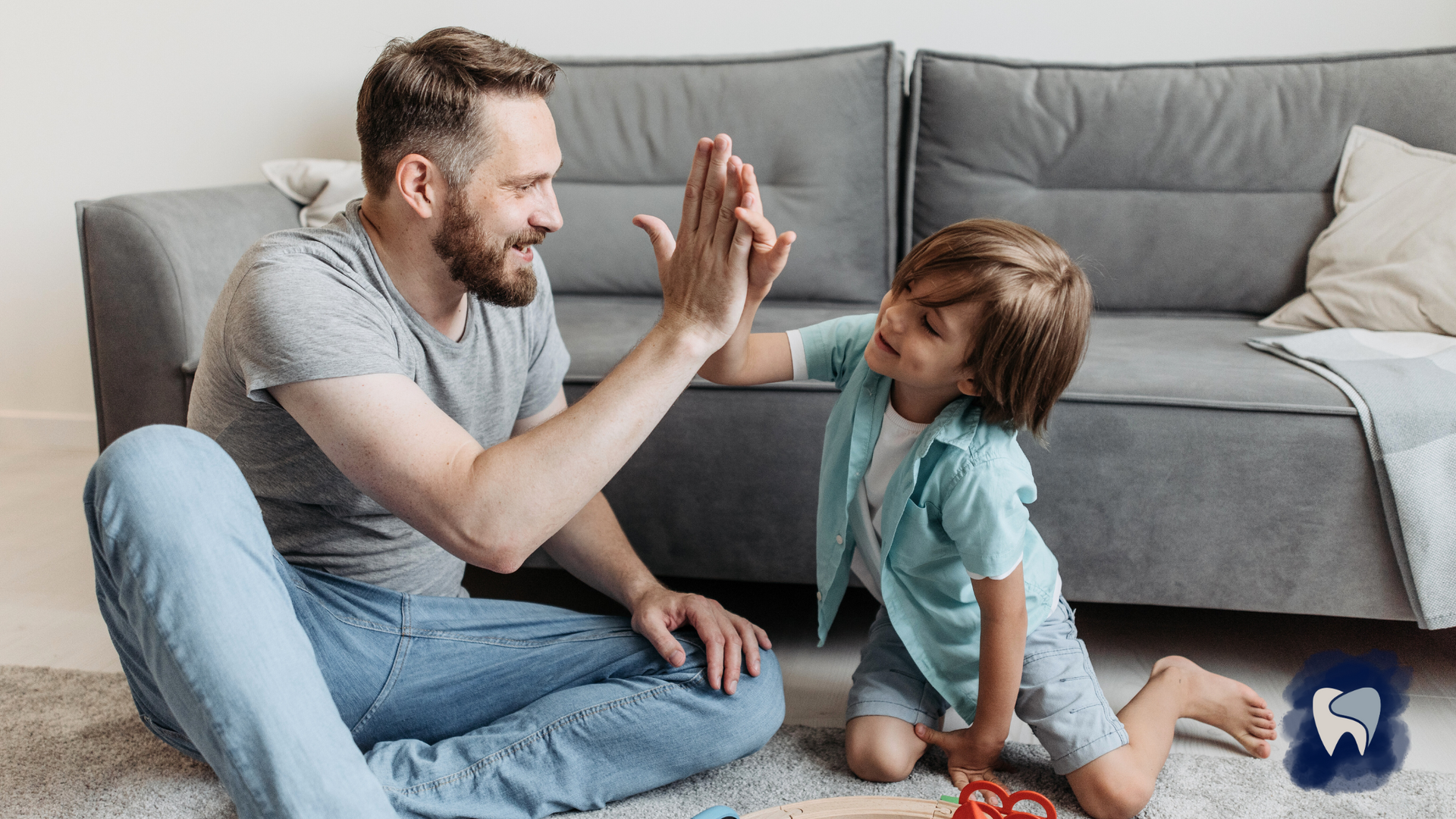 A man and a boy are sitting on the floor giving each other a high five.