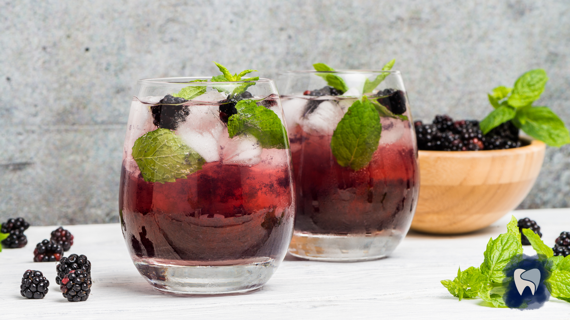 Two glasses of blackberry drink with ice and mint leaves on a table.