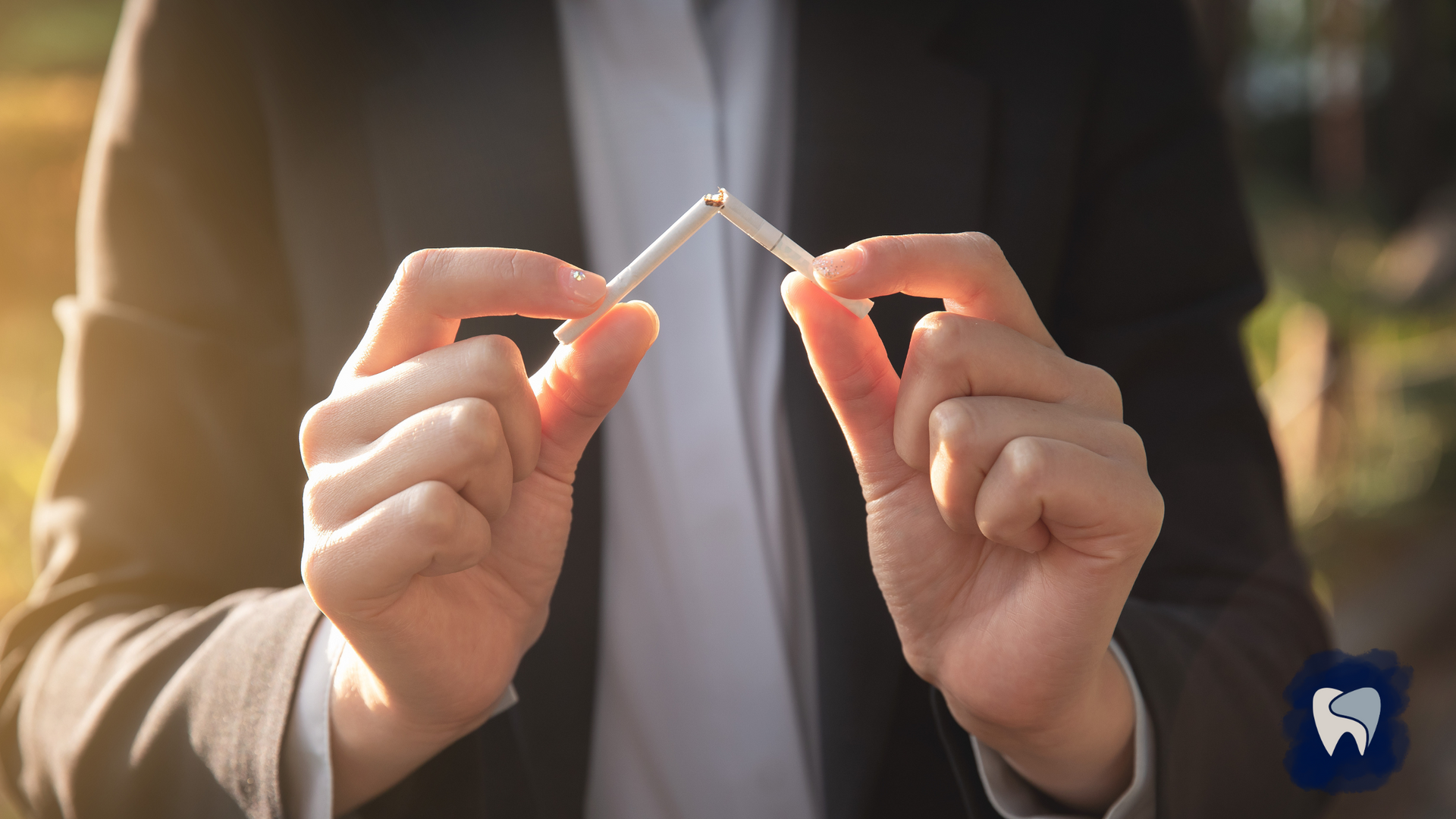 A man in a suit is holding two cigarettes in his hands.