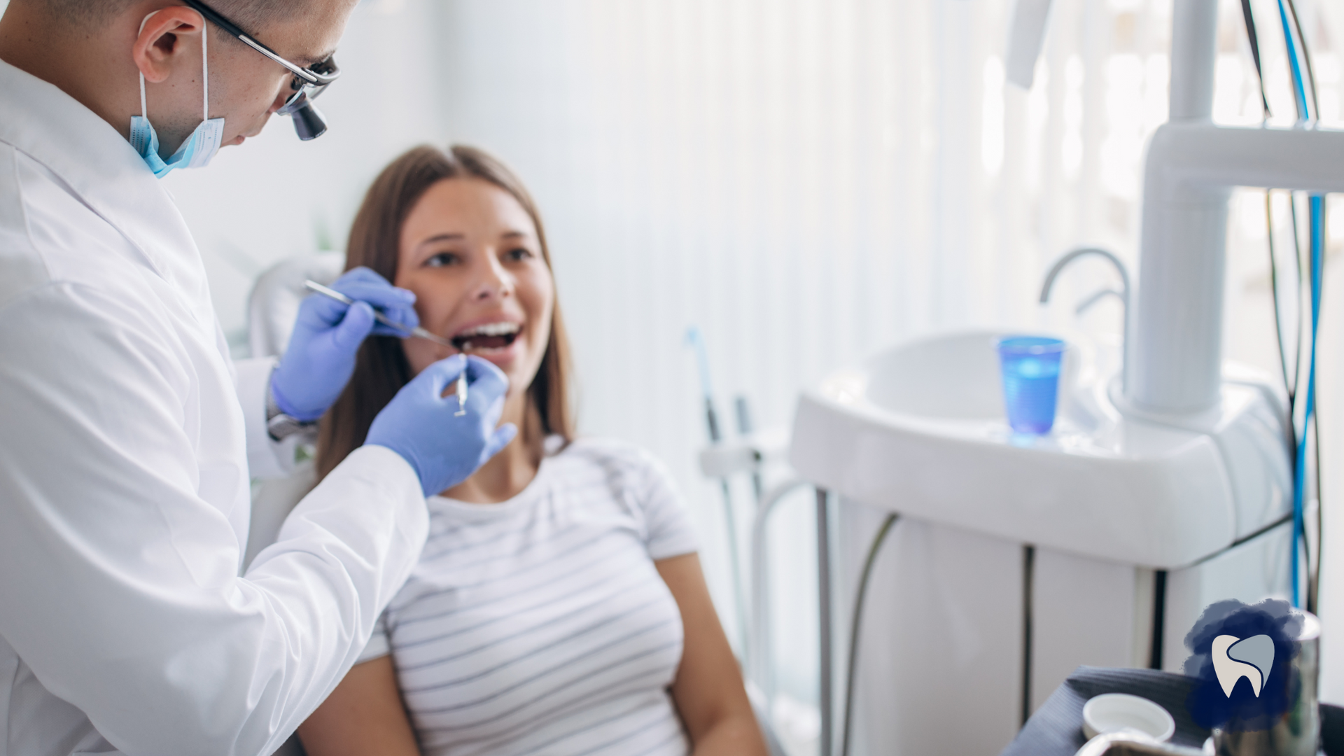 A woman is sitting in a dental chair while a dentist examines her teeth.