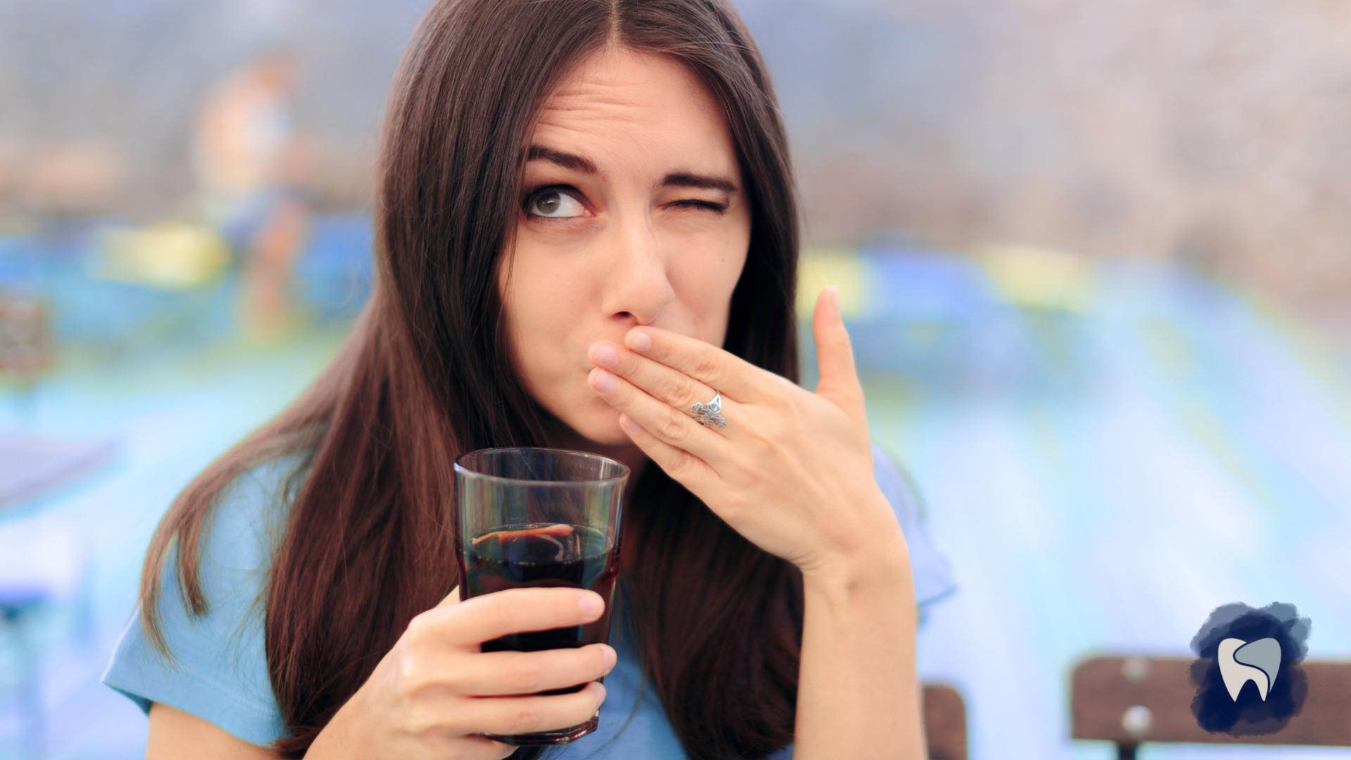 A woman is drinking a glass of soda and covering her mouth with her hand.