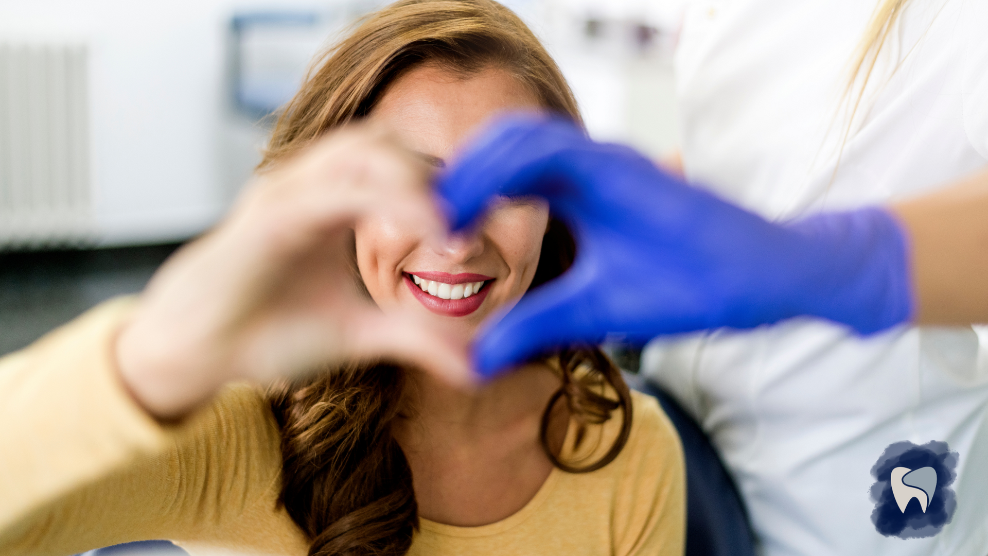 A woman is making a heart shape with her hands in a dental office.