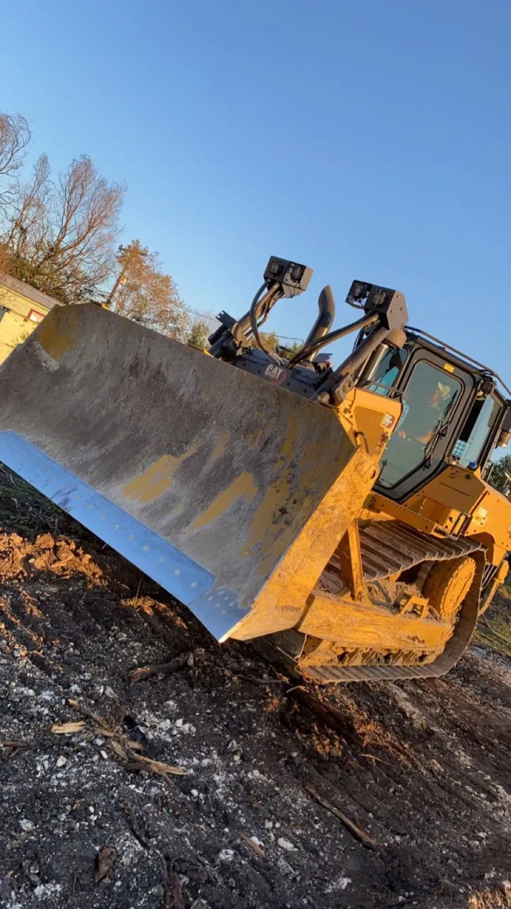 Bulldozer pushing earth, yellow and tan, in a dirt setting with clear blue sky in background.