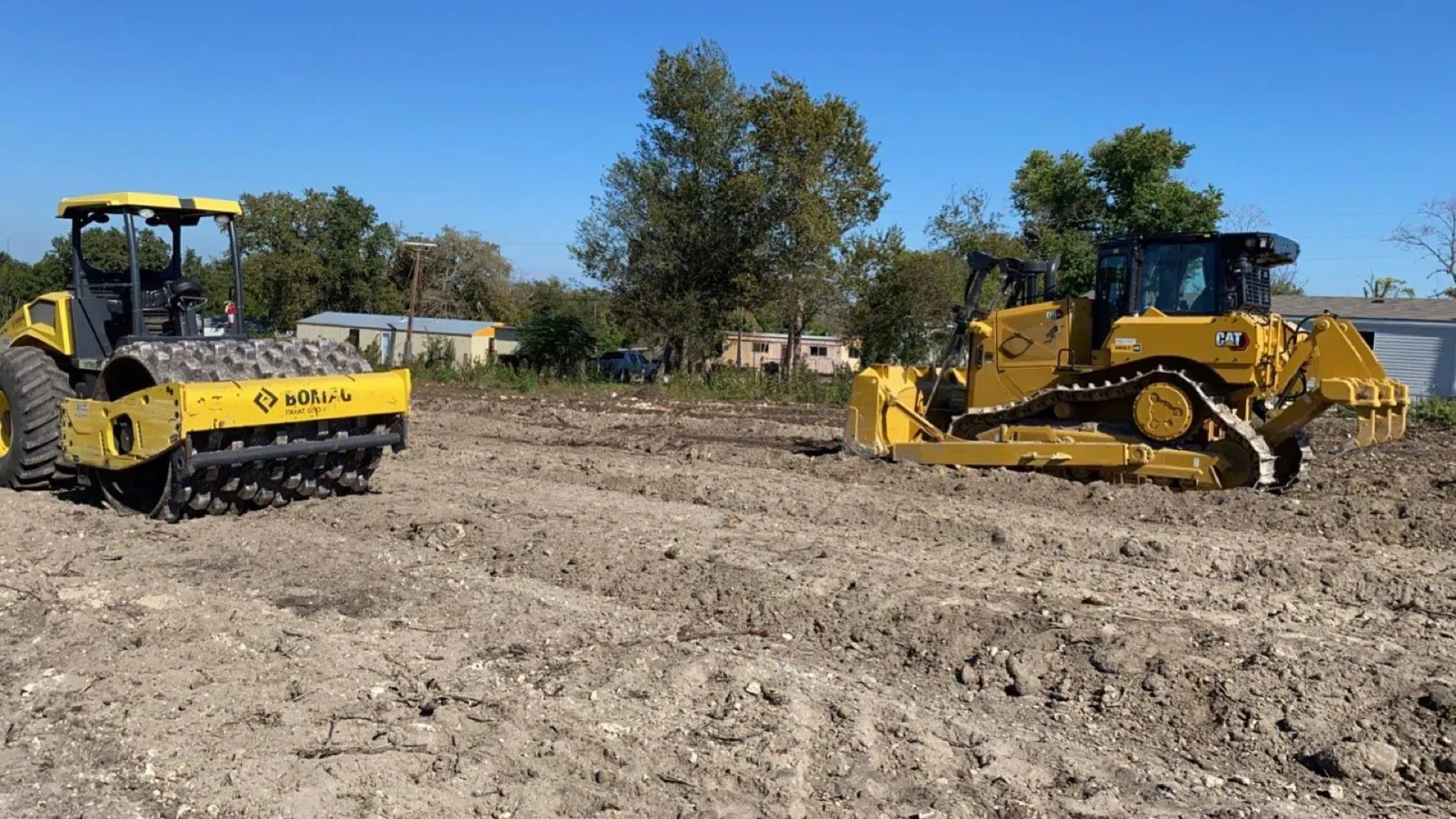 Yellow construction equipment compacts soil on a sunny day.