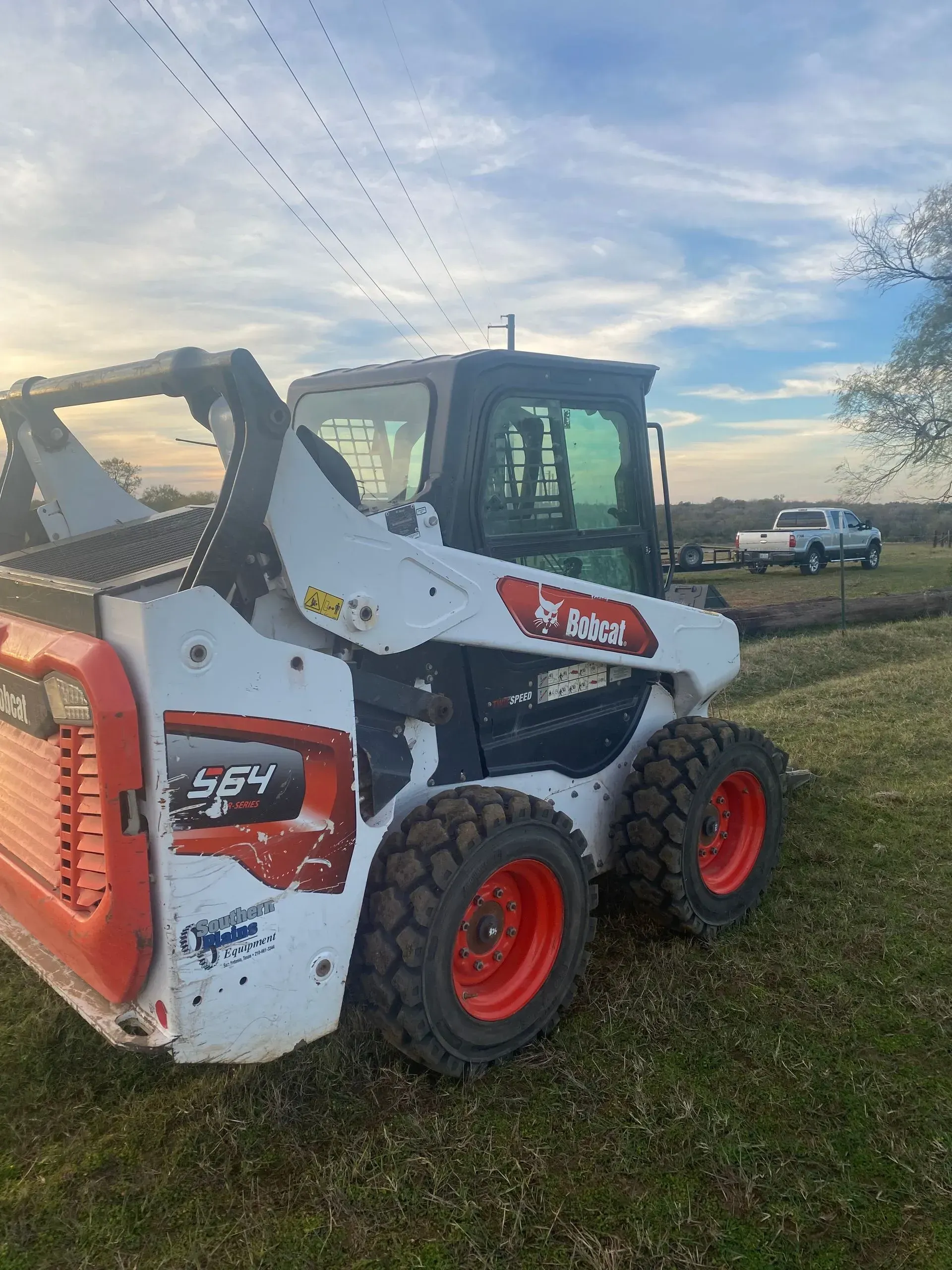 White Bobcat skid-steer loader on grass, orange wheels, cloudy sky.