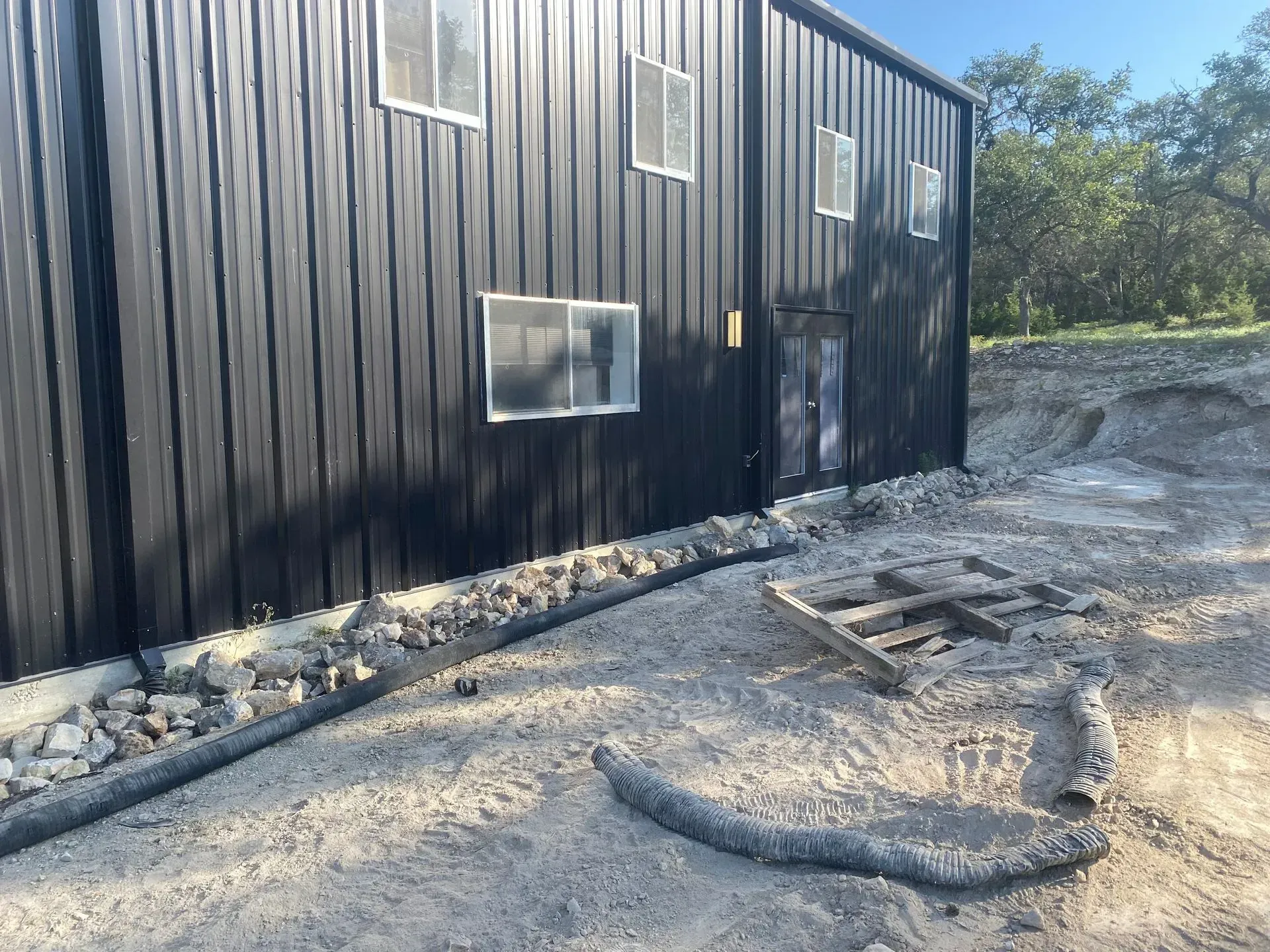 Black metal building with windows, door, and a gravel border.