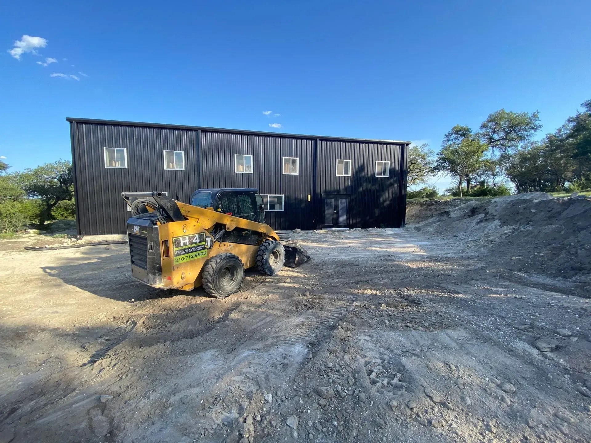 A black metal building with a skid steer in front on a gravel area under a blue sky.
