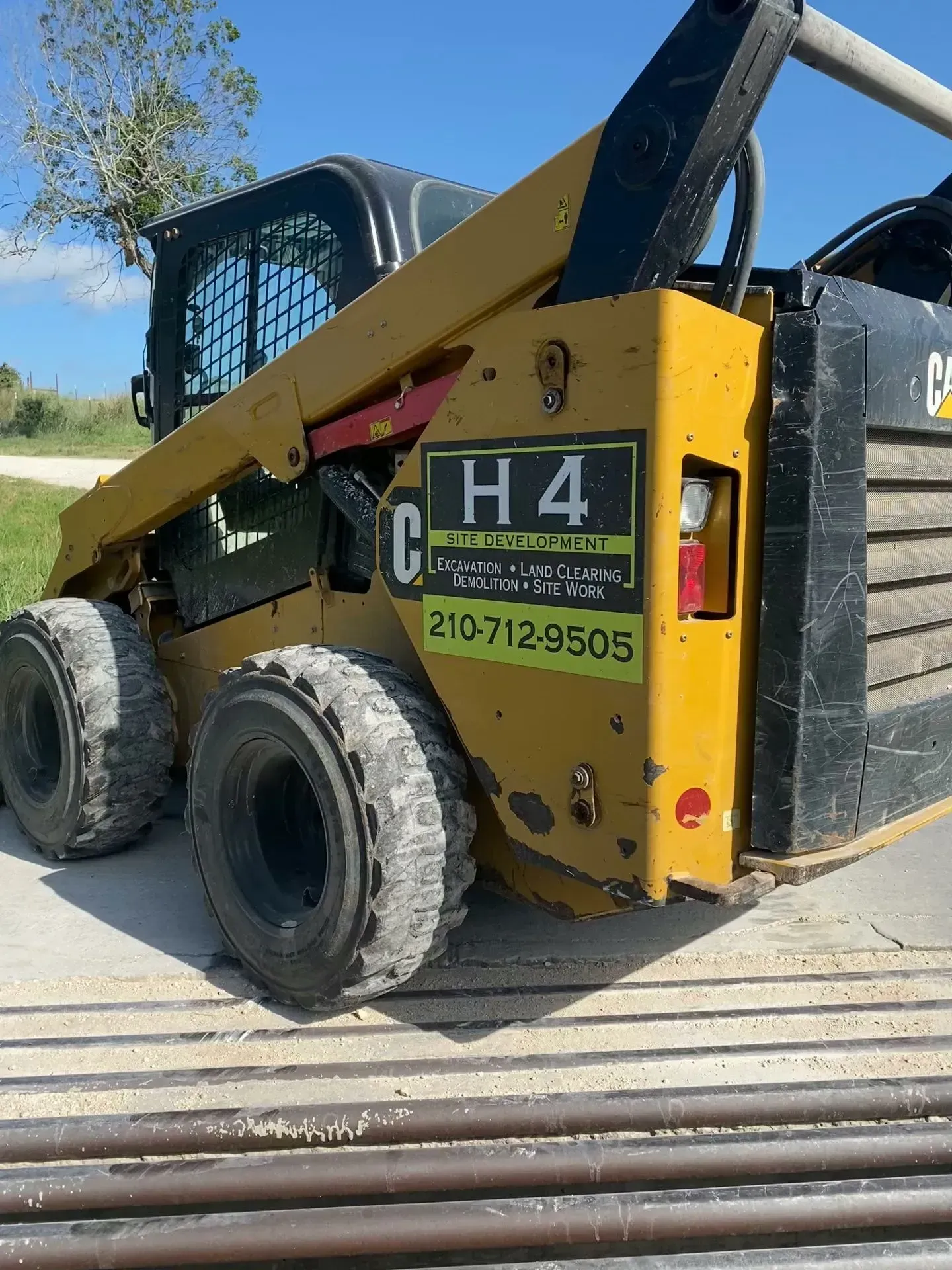 Yellow Caterpillar skid steer loader with black attachments; H4 sticker with a phone number.