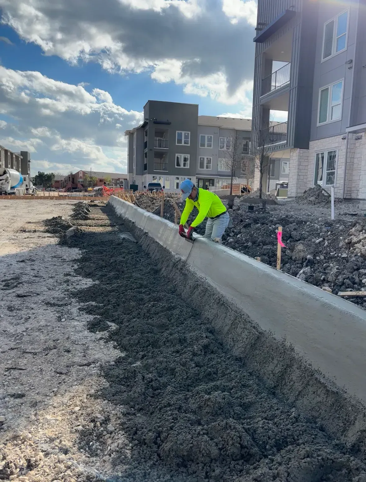 Construction worker in yellow vest cuts concrete curb with a saw on a sunny day.