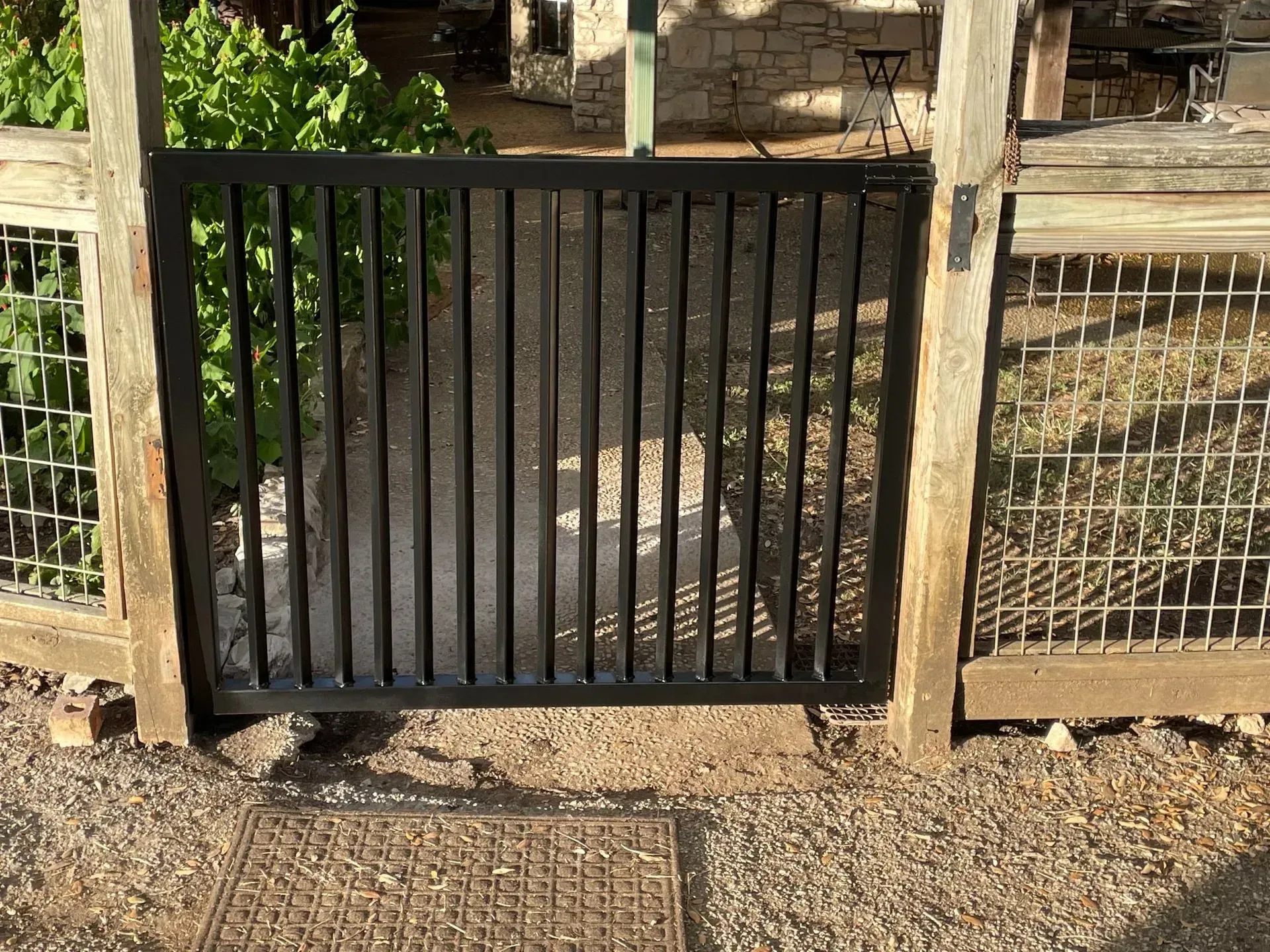 Black metal gate between wooden posts, set in a dirt path.