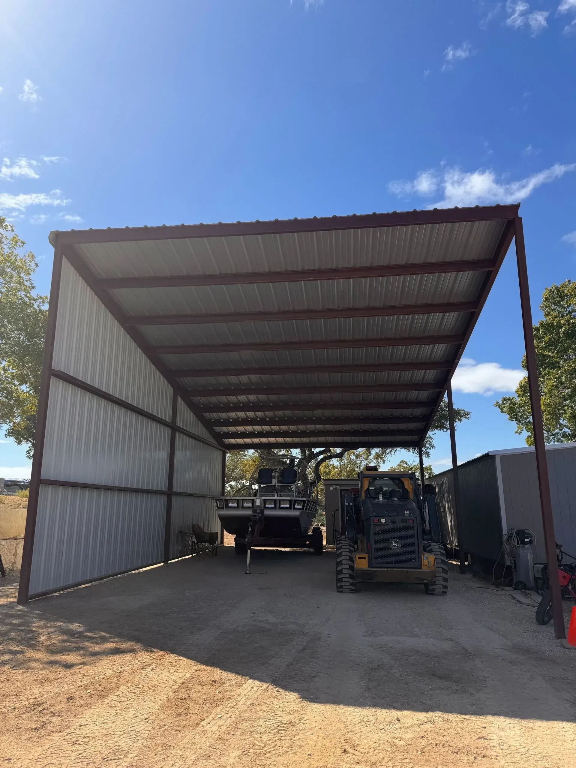 Metal shed with equipment parked inside under a blue sky.