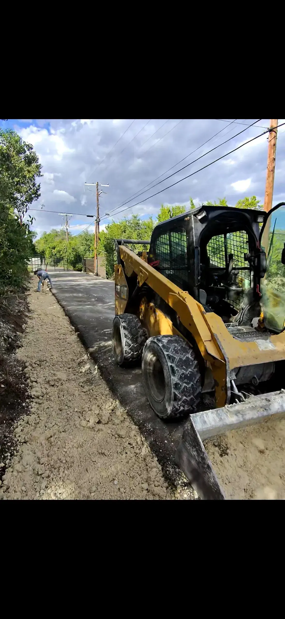 Yellow skid steer on a freshly paved road, under a cloudy sky.