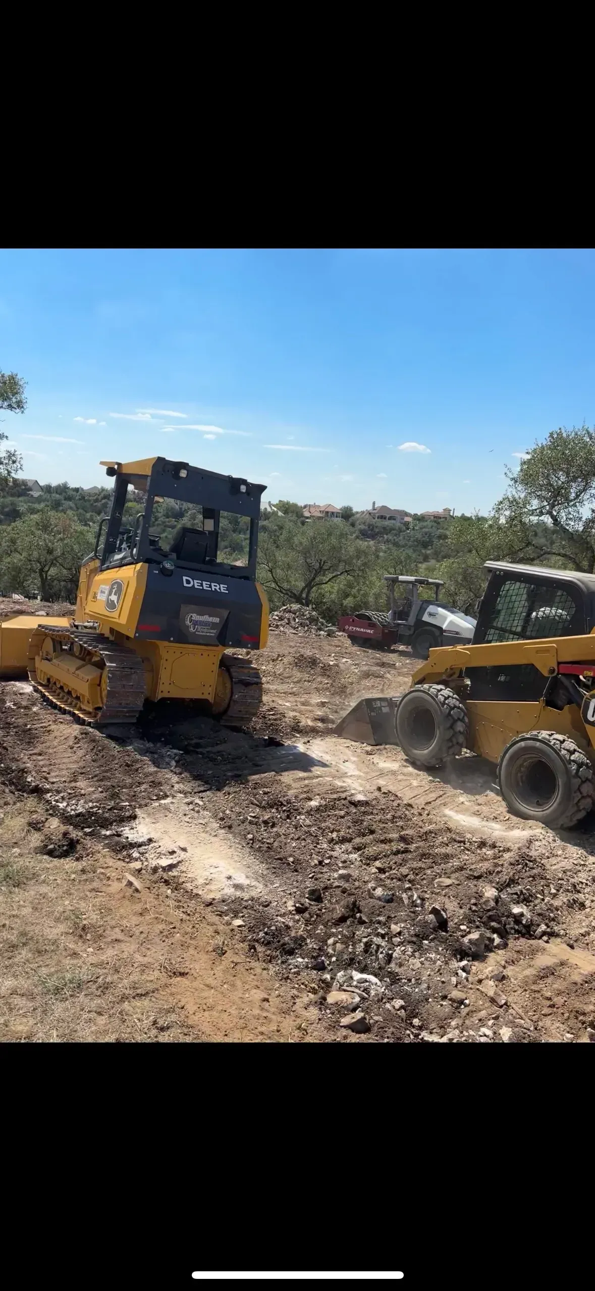 Two yellow bulldozers on a dirt lot, clearing land under a blue sky.