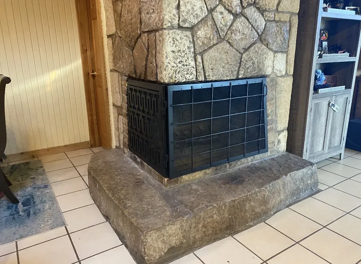 Stone fireplace with black metal door on a tiled floor.