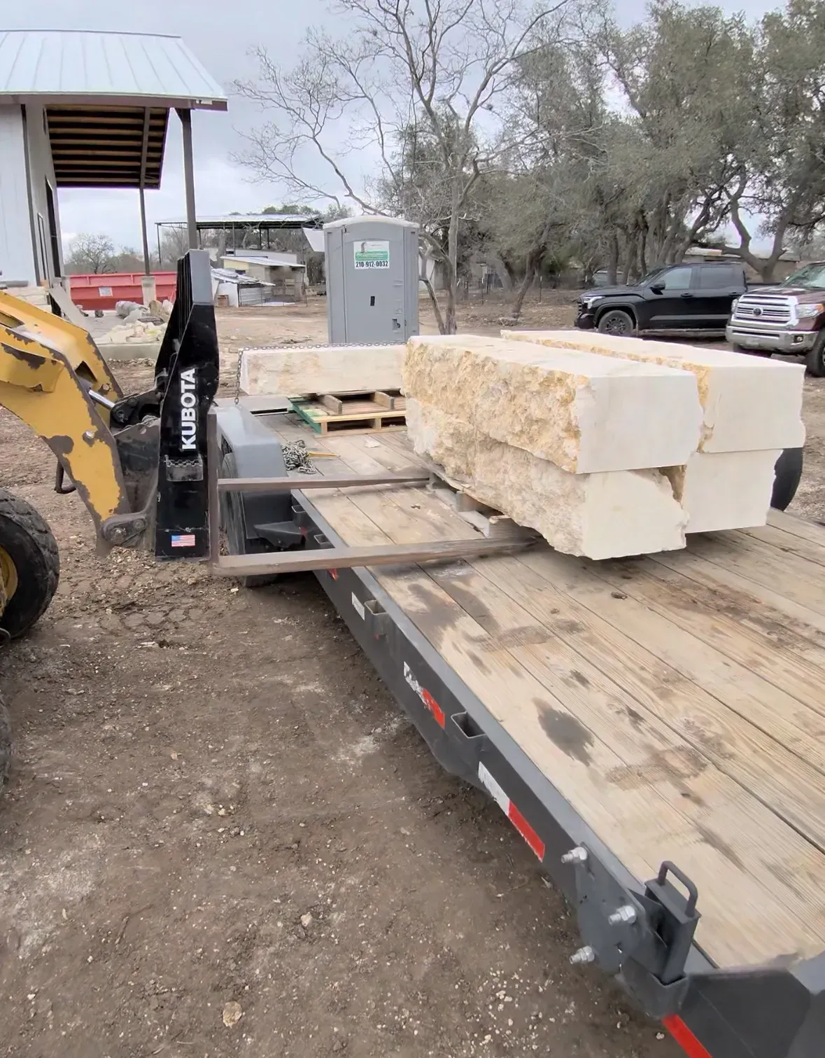 Yellow loader with stone blocks on a trailer in an outdoor construction setting.