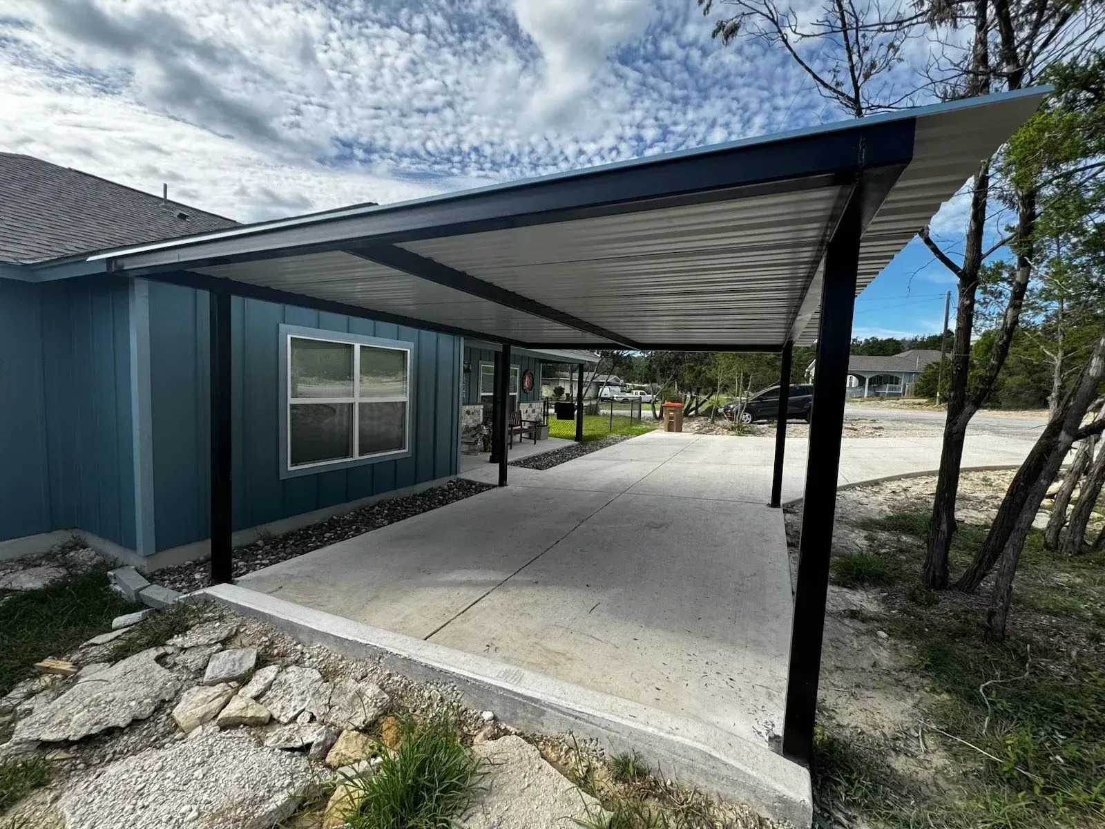 Blue house with a concrete patio covered by a black-framed awning.