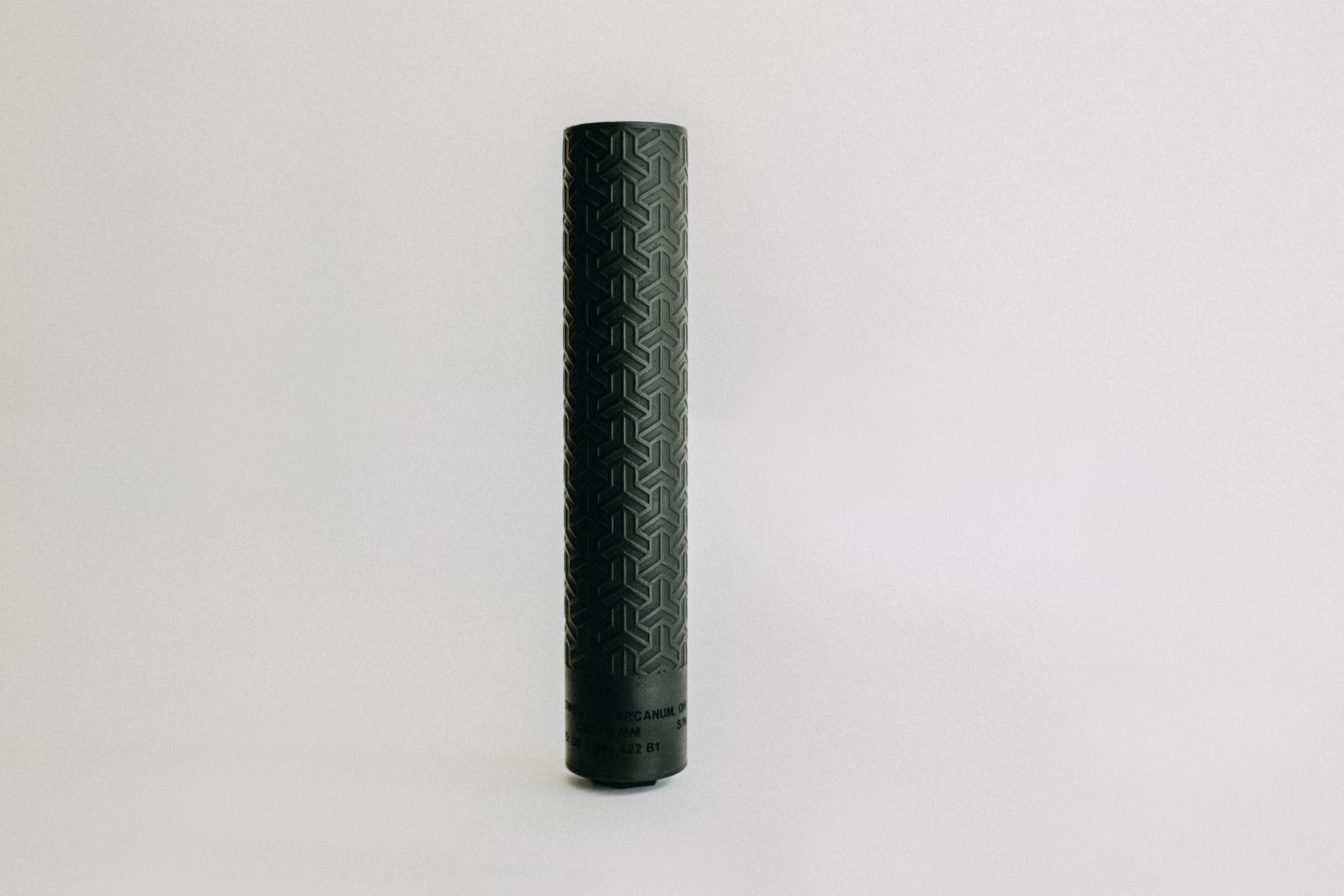 A black cylinder with a pattern on it is sitting on a white surface.