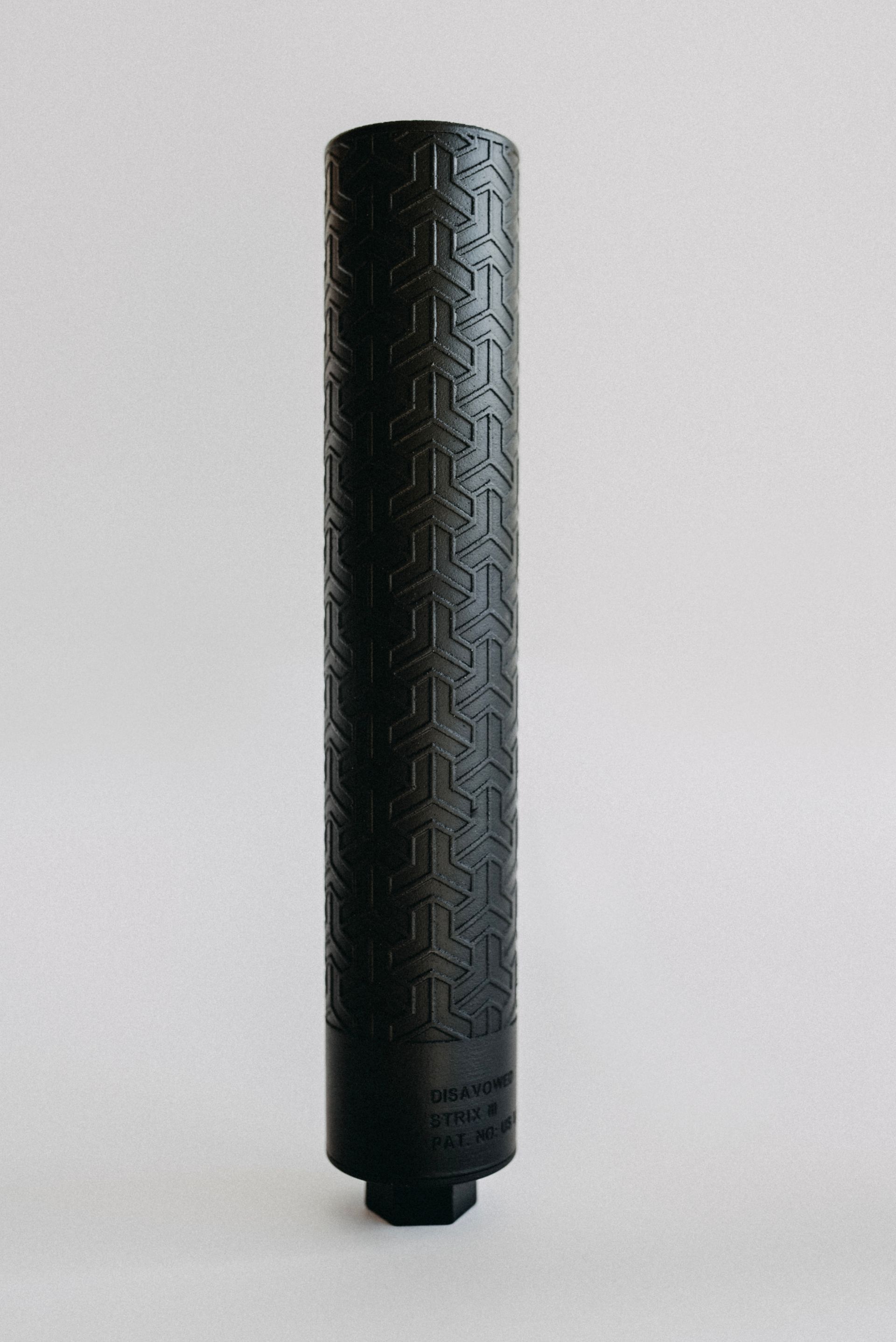 A black cylinder with a pattern on it is sitting on a white surface.