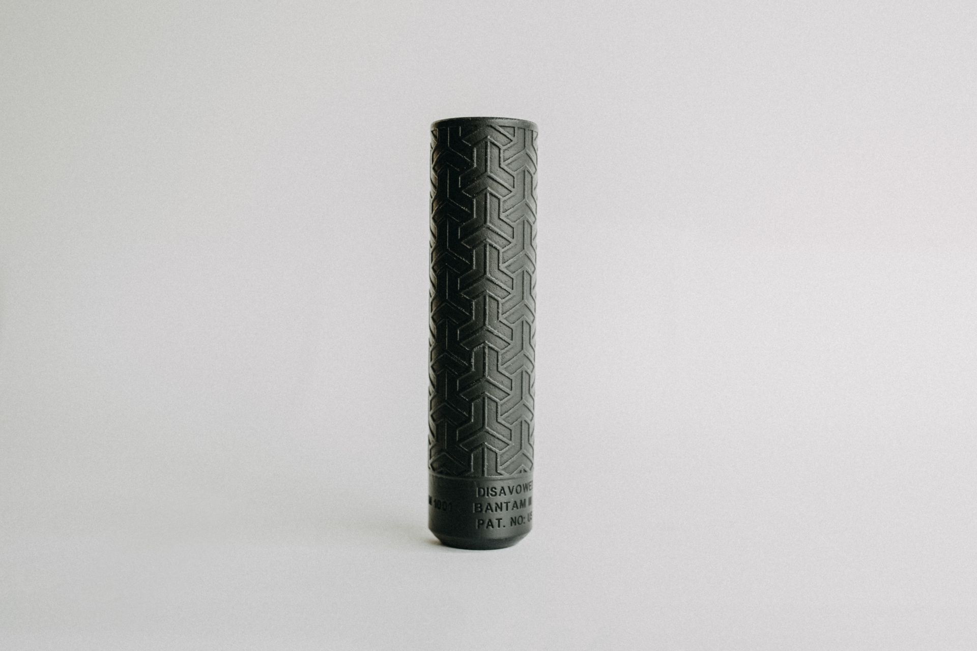 A black cylinder with a pattern on it is sitting on a white surface.