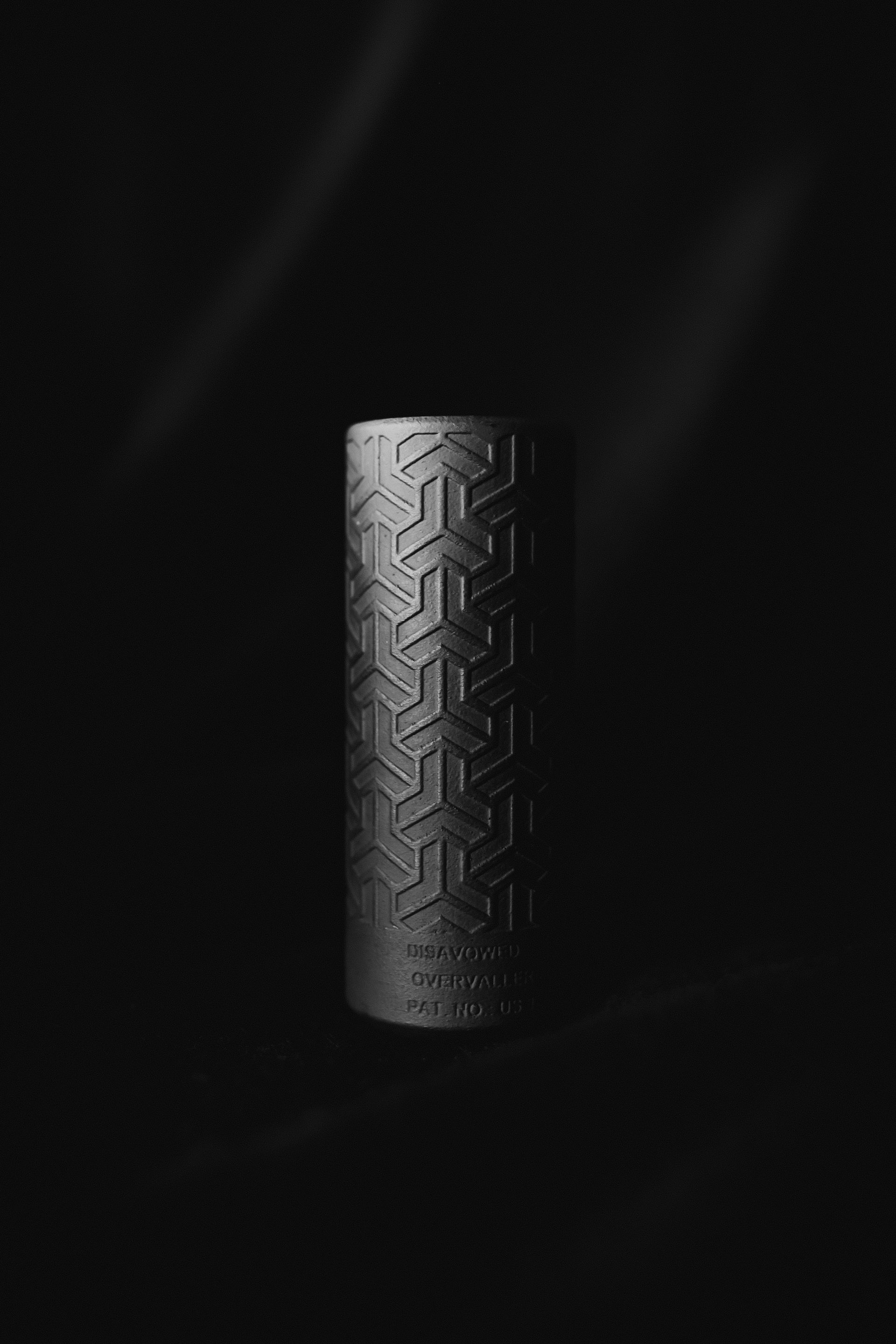 A black cylinder with a pattern on it is sitting on a black surface.