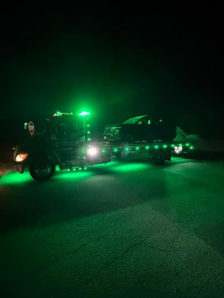 A tow truck with green lights hauling a vehicle at night.