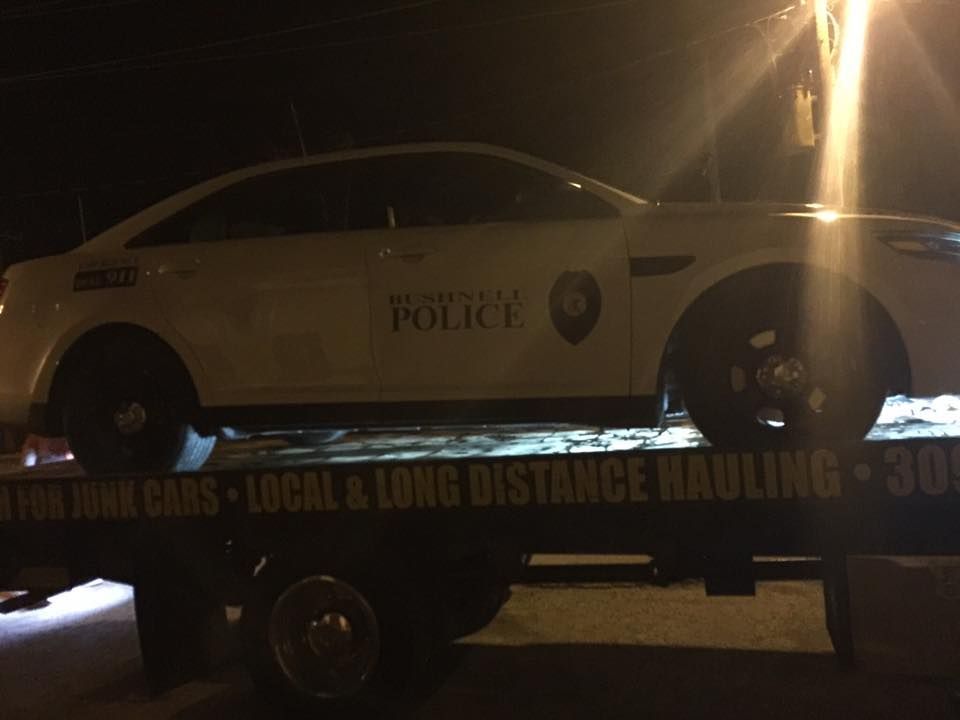 Police car on a tow truck at night, text on tow truck reads 