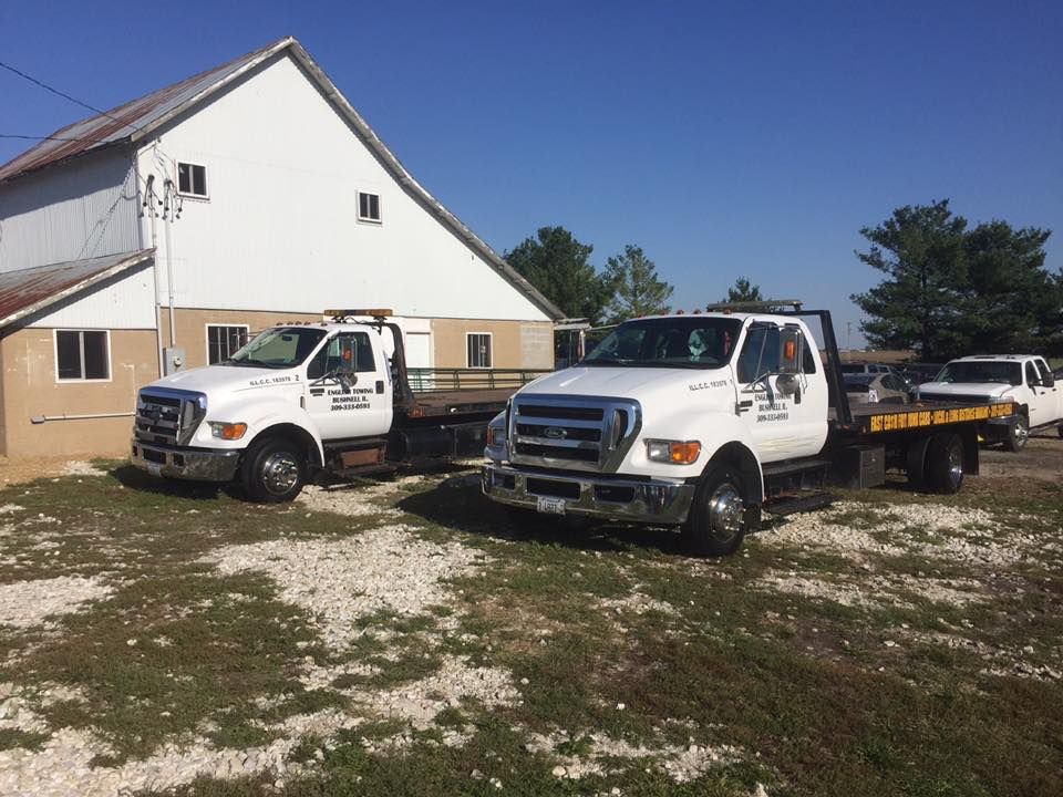 Two white tow trucks parked next to a white building on a sunny day.