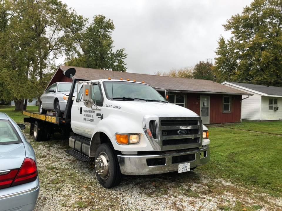 Tow truck with a car on its flatbed in front of a house on a cloudy day.