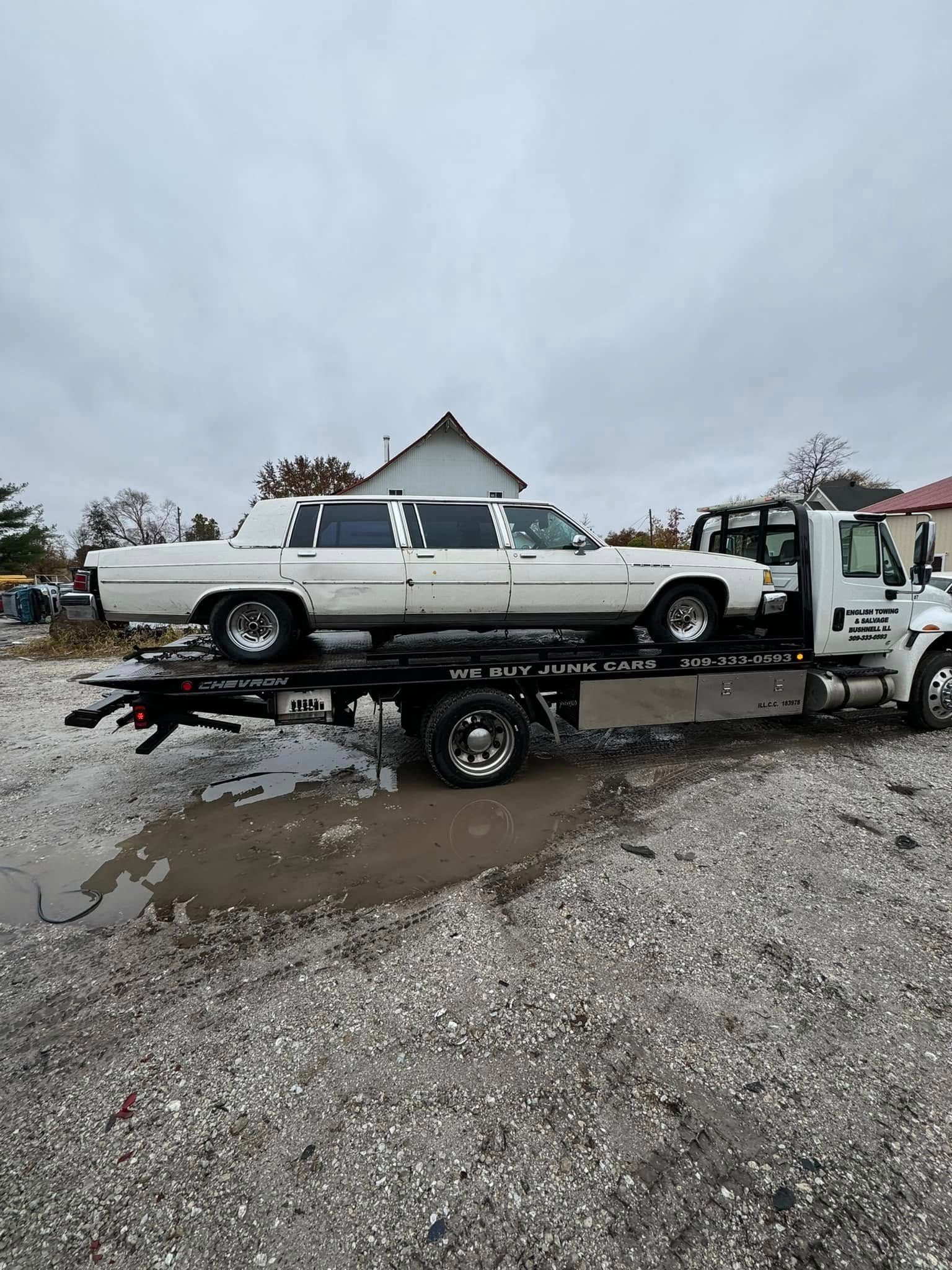 White limousine on a flatbed tow truck outdoors on a cloudy day.