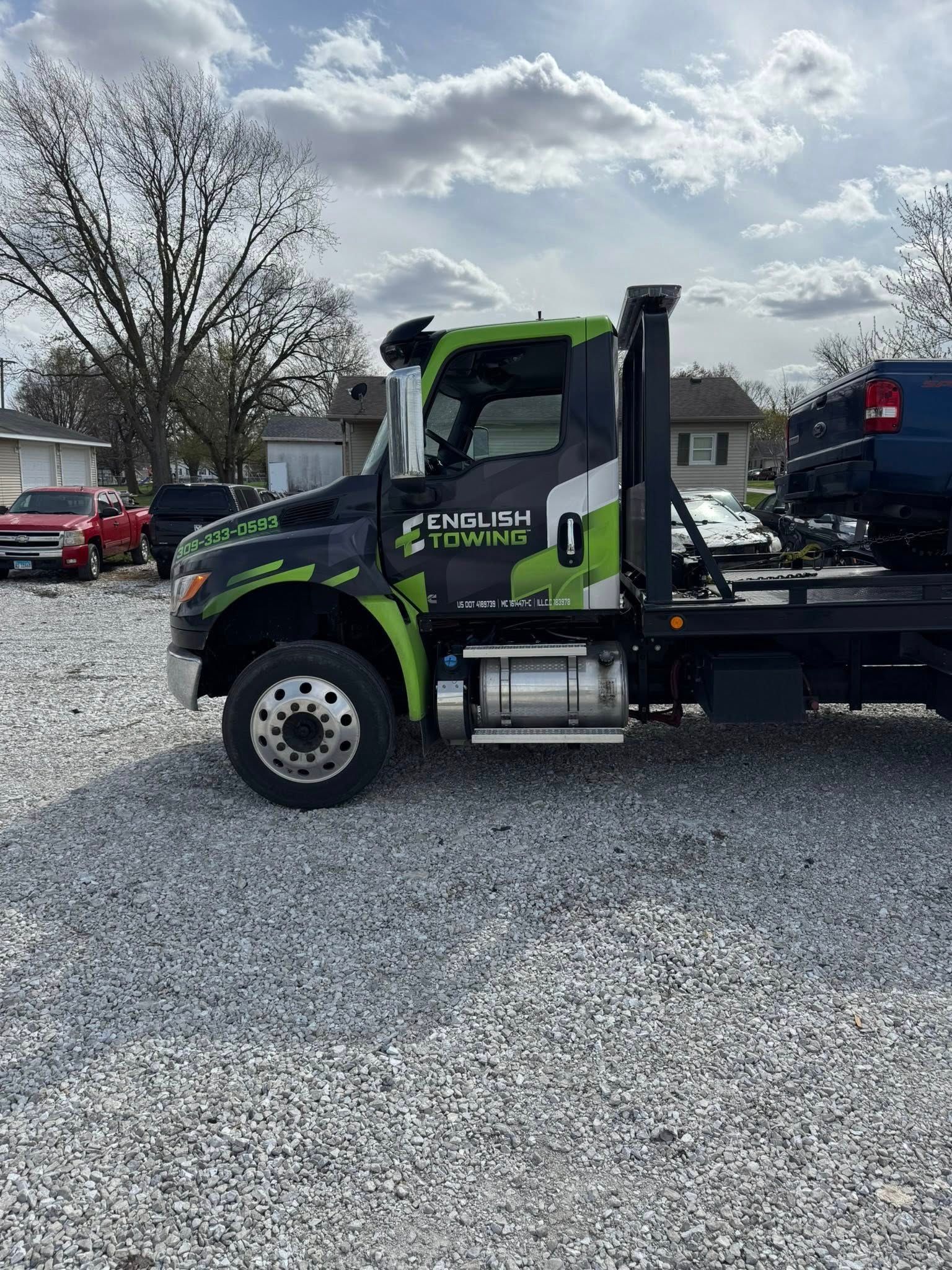 Towing truck with black and neon green wrap parked on gravel. Cloudy sky in the background.