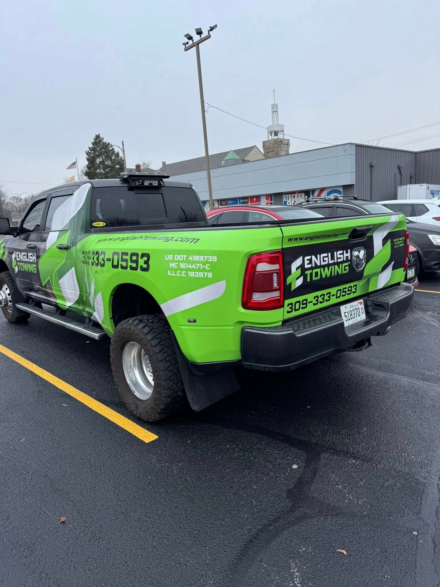 Green and black tow truck in a parking lot, displaying company information on its side.